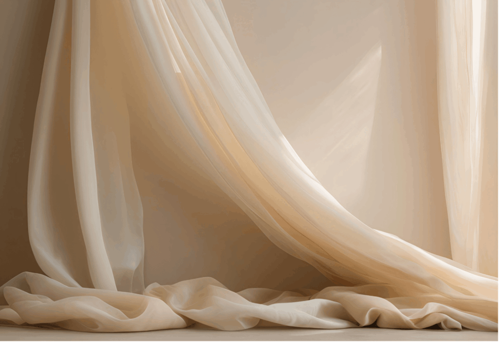 Ein sanfter, transparenter Stoff in einem hellen Cremeton oder Champagnerfarbe drapiert sich elegant von oben nach unten und bildet weiche Falten und Schatten auf einer hellen Oberfläche.