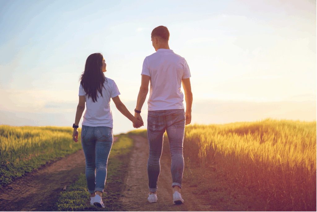 Ein Paar geht bei Sonnenuntergang Hand in Hand einen Feldweg entlang, umgeben von goldenen Feldern.