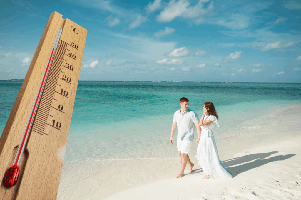Hochzeitspaar spaziert barfuß am tropischen Strand entlang bei sommerlicher Hitze mit sichtbarem Thermometer