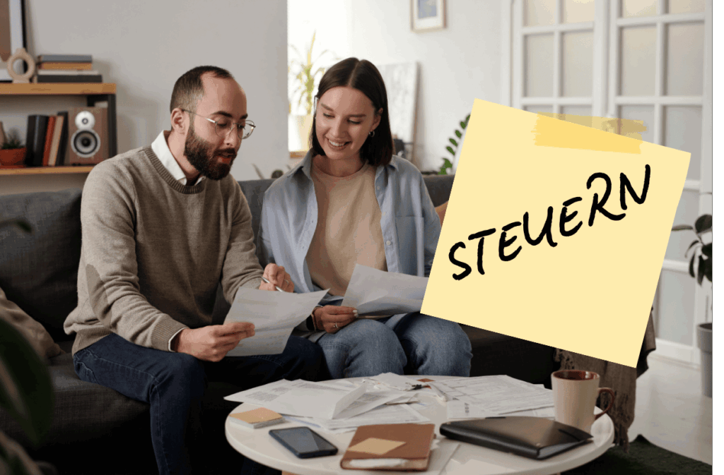 Ein glückliches Ehepaar sitzt auf einem Sofa und bespricht Dokumente, mit Notizen und Unterlagen auf dem Tisch, während ein Post-it mit dem Wort "STEUERN" (Steuern) prominent im Vordergrund ist.