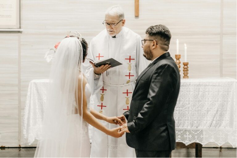 Bei einer Hochzeitszeremonie spricht ein Priester den Trauspruch, während das Brautpaar sich an den Händen hält.