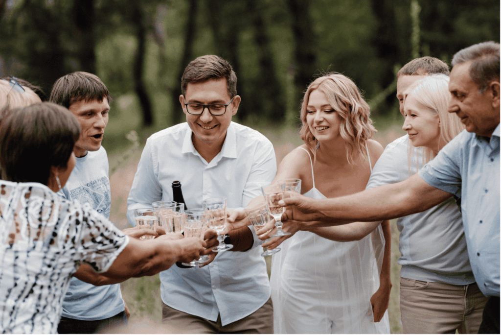 Eine Gruppe von Freunden und Familie stoßen mit Sektgläsern an, um die Verlobung zu feiern. Die zukünftige Braut strahlt in der Mitte.